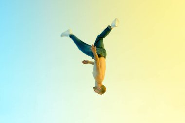 Eğilimli esnek tişörtsüz erkek sporcunun modern stüdyoda arka planda hafif arka plana ters takla atması.