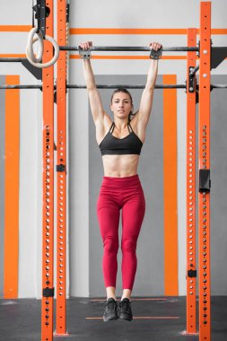 Formda atletik bir kadın sağlıklı ve aktif bir yaşam tarzı için Crossfit spor salonunun barlarında ölü gibi takılıyor.