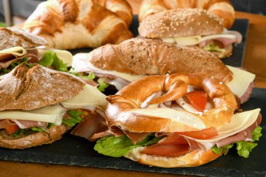High angle of assorted appetizing sandwiches with ham cheese and veggies served on slate boards on wooden table in restaurant