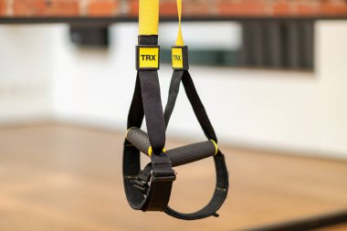 Yellow TRX ropes with black handles hanging on blurred background of gym during suspension training