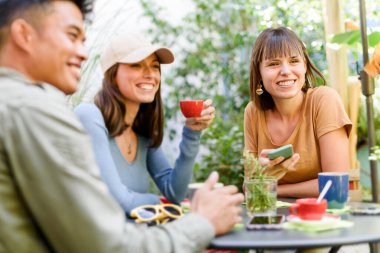 Carefree friends sitting at table with cups of coffee and chatting with each other in outdoor cafe