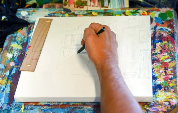 From above anonymous man drawing sketch of house on canvas while working in creative studio