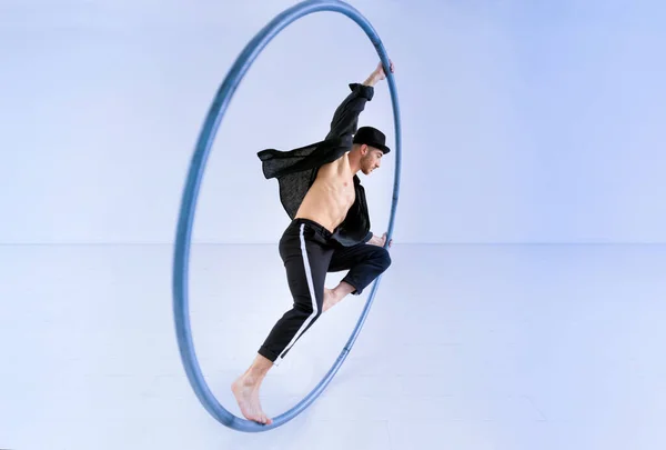 Full body barefoot man in costume doing trick on cyr wheel against blue background during acrobatic performance