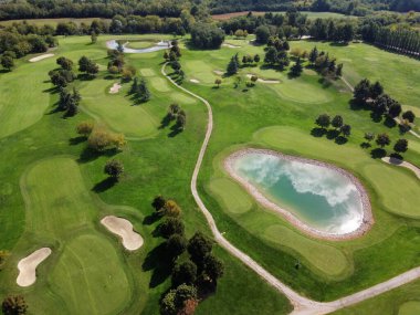 Yolları ve bakımlı ağaçlar arasında küçük göleti olan yemyeşil yemyeşil golf sahası
