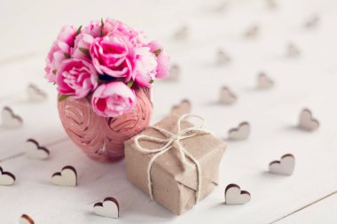 Güzel bir vazoda küçük pembe güller ve kraft kağıdına sarılmış küçük bir hediye. Tatil kavramı