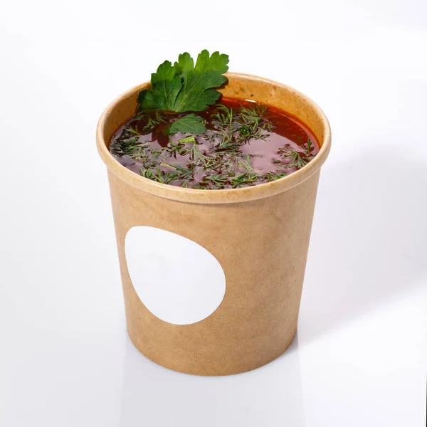 Ukrainian national cuisine - red borsch with vegetables, meat and dill. Sour soup in a paper cup on a white background. Close up. Ukrainian menu.