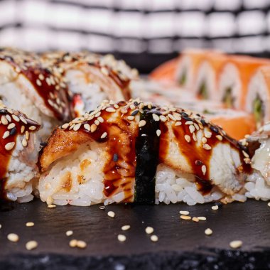 Susam tohumları serpiştirilmiş ve üzerine sos serpiştirilmiş siyah bir tahta üzerine uzanmış bir nigiri sushi 'ye yaklaş. Suşi rulolarının yaratıcı sunumu kavramı.