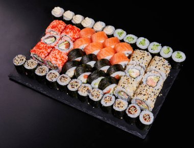 Büyük bir suşi seti. Siyah bir tabakta taze dolgular var. Nigiri, maki ve uramaki 'li menü suşisi. Restoran veya teslimat siparişi vermek için..