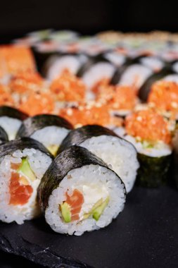 Siyah arka planda somon, avokado ve krem peynirle doldurulmuş Maki ruloları. Seçici odaklanma. Bulanık arkaplan.