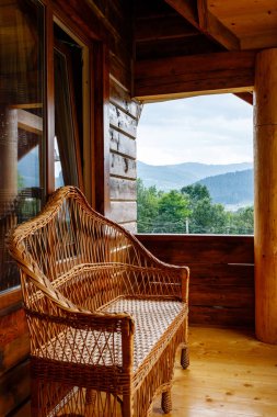 Ahşap balkonda hasır banklı, dağ manzaralı güzel bir teras. Hasır ürünler. Dağlarda dinlenmek için ahşap kulübenin dekoratif unsurları..