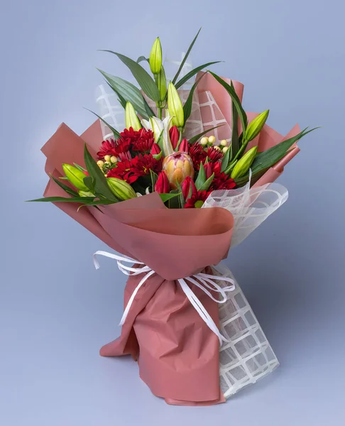 Festively packed bouquet with red chrysanthemums and white lilies that have not yet bloomed. Concept of floristics and composing greeting bouquets.