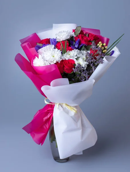 Bouquet of pink and white flowers wrapped in floral paper on a blue background. Original beautiful bright bouquet with red roses, white chrysanthemums and blue irises. Concept of giving flowers.