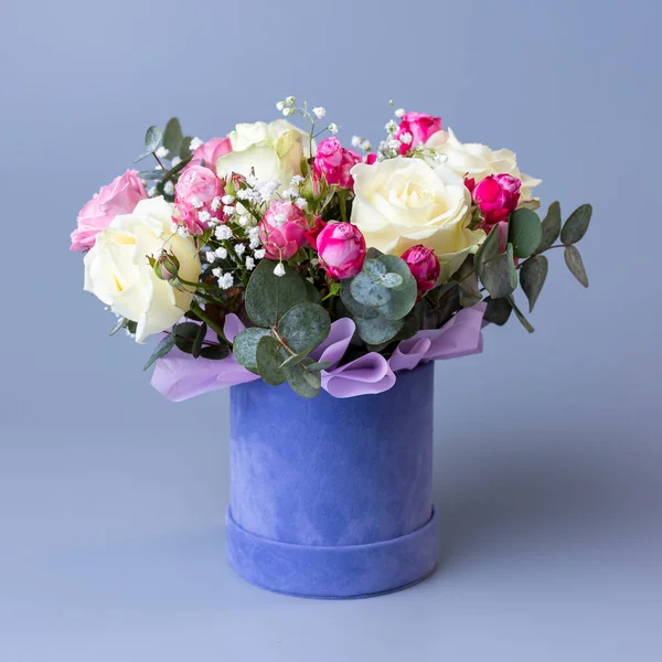 Bouquet in a blue velor round gift box on a blue background. Original bright bouquet with beige and pink roses, white gypsophila and eucalyptus twigs. Concept of floristics.