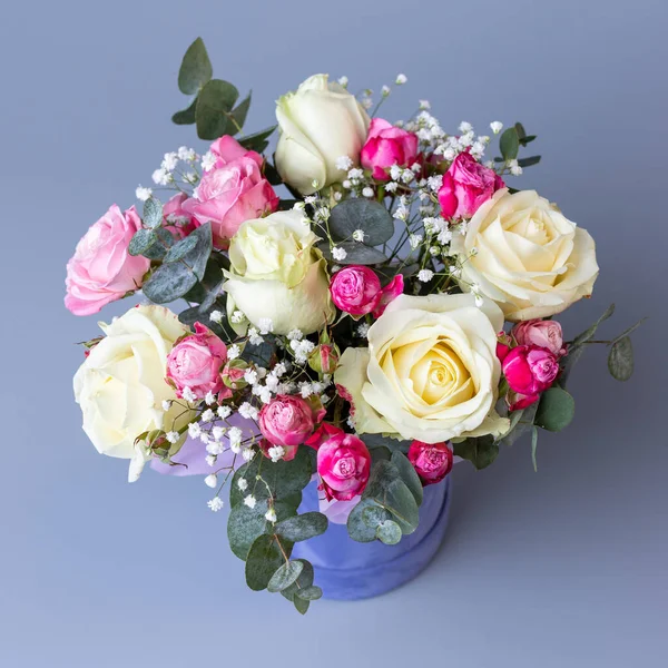Bouquet in a blue velor round gift box on a blue background. Original bright bouquet with beige and pink roses, white gypsophila and eucalyptus twigs. Floral banner.