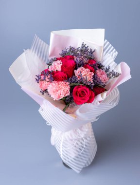 Bouquet of red and pink flowers wrapped in festive paper on a blue background. Festively packed bouquet in red and purple colors. Concept of Womens Day, Mothers Day and Birthday.