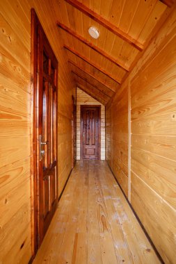 Bright minimalist corridor with a sloping ceiling in which the entrances with massive doors to the rooms in a wooden cottage.