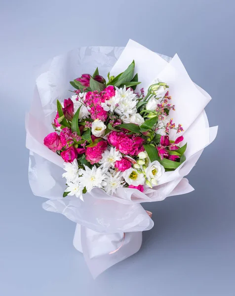 Big bouquet of pink and white flowers wrapped in bright floral paper on a blue background. Festively packed bouquet with pink peonies, white chrysanthemums and eustoma. Concept of floral arrangements.