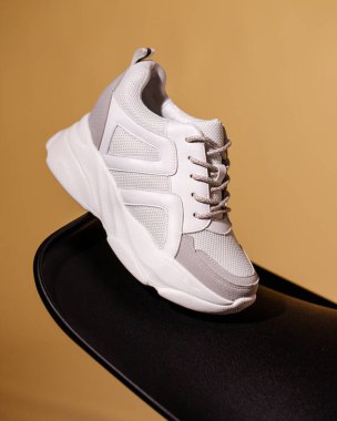 One white womens sneakers on black podium on beige background. Side view close up of new collection of sports shoes on studio background. Advertising banner. Copy space.