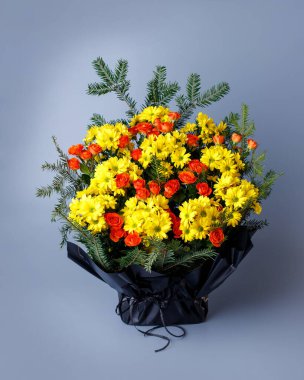 Original bouquet of small pink roses, yellow chrysanthemums and spruce twigs. Bouquet wrapped in black floral paper with ribbon standing on a blue background. Concept of floristics.