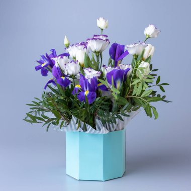 Bouquet of eustoma in a turquoise cardboard gift box on a blue background. Original bright bouquet with white eustoma, tulips, purple irises and sprigs of greenery. Concept of floral arrangements.