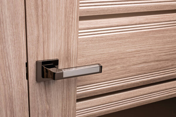 External door handle without protective lock on wooden frame. Close up of metallic door handle on brown front or interior door. Home door design choice concept.