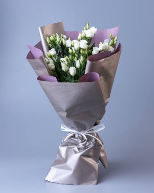 Large festive bouquet of white eustoma stands on a blue background. Flowers are wrapped in double-sided paper and tied with ribbon. Concept of floral arrangements for greetings.