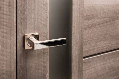 Close up of stylish silver chrome door handle on modern interior door. Stylish light brown door with frosted glass inserts. Concept of catalog of door handles for furniture store.