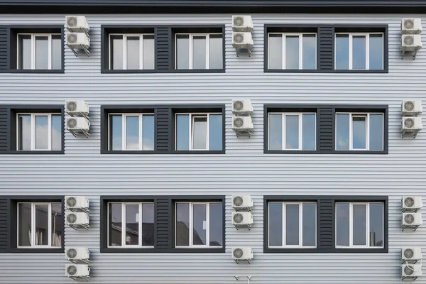 House airconditioning. Many air conditioners hang on facade of new modern building. Central air conditioning fans are neatly arranged on outside wall of white-gray minimalist house or business center.