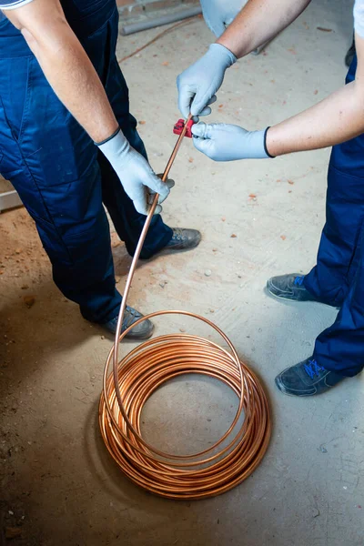 Installation works. Two men in blue overalls and protective gloves prepare underfloor heating for water heating on construction site. Construction work concept.