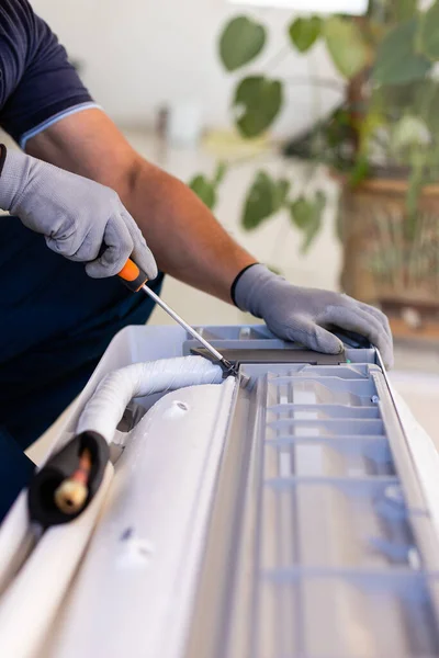 Preparation for installation of conditioning equipment. Male technician hands using screwdriver fixing modern air conditioner indoors. Close up of worker's hands and screwdriver. Selective focus.