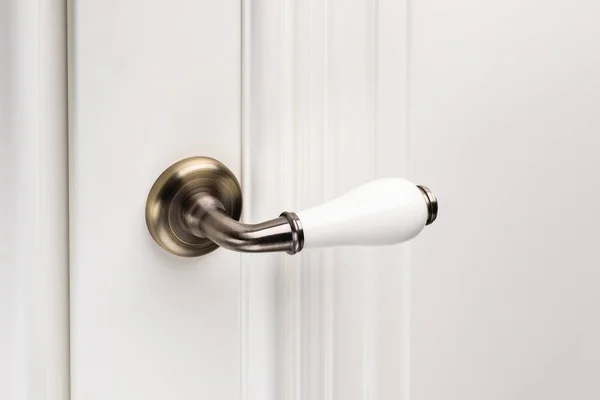 Close up of stylish and elegant door knob or handle on white door. Vintage white and bronze door handle on door that is suitable for refined home interior. Details concept.