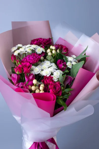 Bouquet of pink and white flowers wrapped in floral paper on a blue background. Original beautiful bouquet of pink roses, eustoma and white little asters. Concept of floral arrangements for greetings.