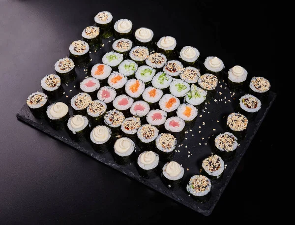 Different types of maki rolls with different fillings lined with a square on a plate on a stone background. Japanese food concept.