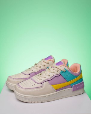 Pair of fashionable bright sports shoes for teens standing on white podium on light green background. Side view of white sneakers with turquoise and purple inserts. Copy space.