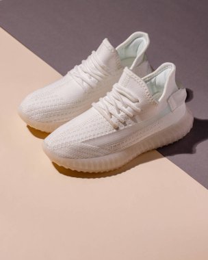 Pair of stylish comfortable sports running shoes on colored background. Close up of original model of white modern women's sneakers standing on beige and gray background. Female sports style concept.