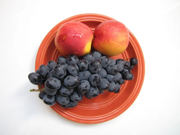 Rijp zwart druiven en twee perziken in oranje keramische plaat geïsoleerd op witte achtergrond — Stockfoto