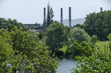 Spring green fresh trees and lake in residential area Drujba against the background of the chimneys of the Thermal Power Plant, Sofia, Bulgaria  