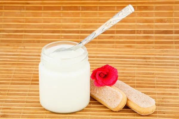 Frasco com iogurte em casa e colher, biscoito e flor — Fotografia de Stock