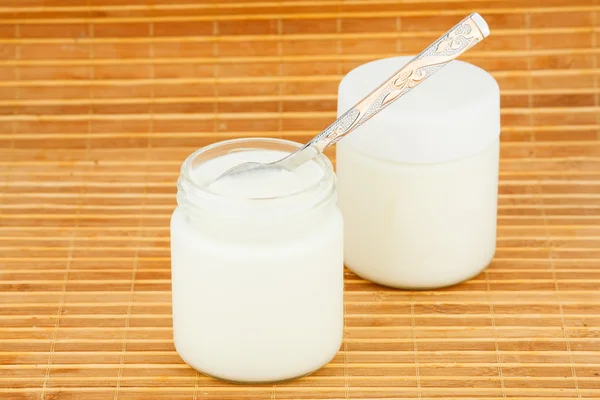 Two jars with home yoghurt and spoon on a straw mat — Stock Photo, Image