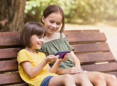 Telefonlarına bakan iki mutlu kız. Parkta internette sörf yapan güzel çocuklar.