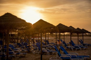 Sahilde güneş yatakları ve şemsiyelerle gün batımı