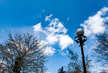 Beyaz bulutlu mavi gökyüzünde sokak lambası ve kuru ağaç