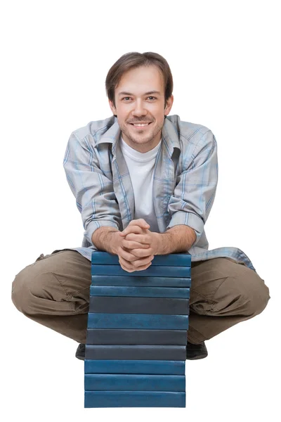 Smiling young man sits behind stack of books — Stock Photo, Image
