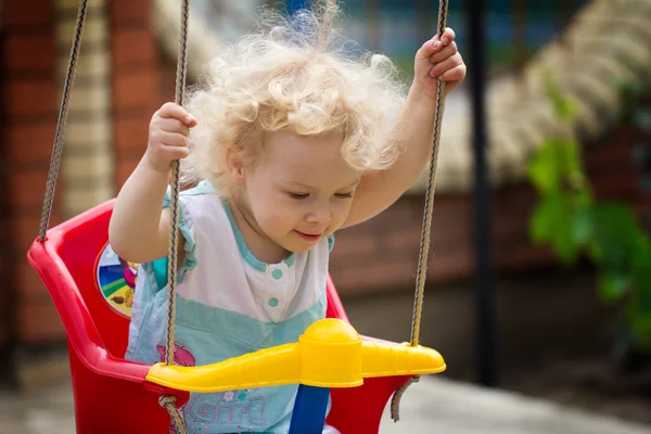 Adorable blonde curly hair little girl having fun on a swing — Stock Photo, Image