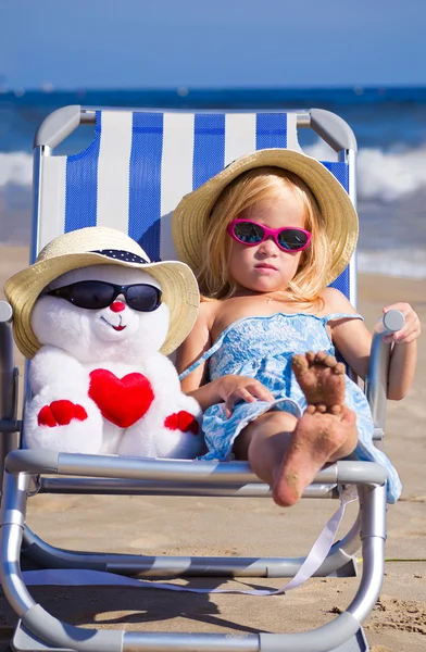 Uma criança senta-se em uma cadeira de praia com um brinquedo — Fotografia de Stock