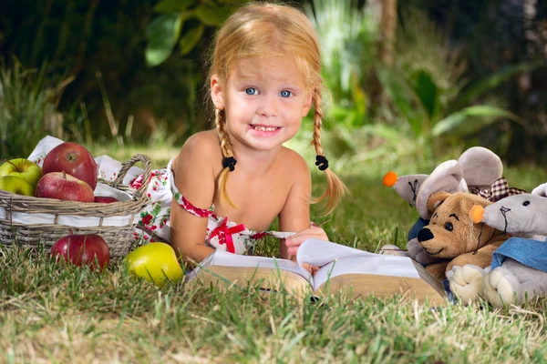 Mädchen liest ein Buch mit Spielzeug im Freien — Stockfoto