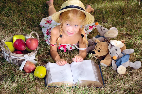 Menina lendo um livro com brinquedos ao ar livre — Fotografia de Stock