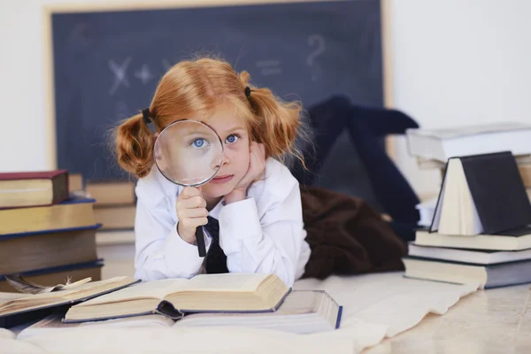 Ragazza si trova con una lente di ingrandimento e libri Immagine Stock