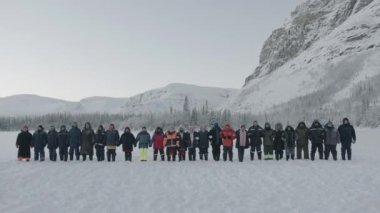 Murmansk bölgesi, Rusya - 10 Ocak 2021: Büyük bir turist grubu sıralanarak aynı anda ormanın ve dağların arka planına karşı karın üzerinde birbirlerine düşüyorlar.