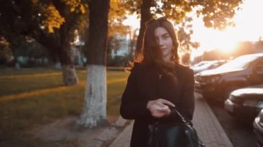 Uzun, lüks saçları olan şık bir genç kız elinde bir çantayla şehir caddesinde dolaşıyor ve gülümsüyor. Yavaş çekim